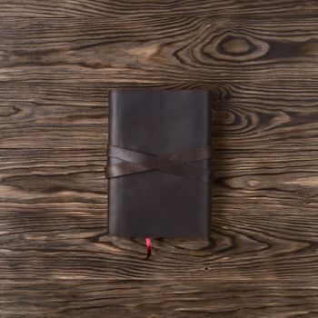 Brown handmade leather notebook cover with notebook on wooden background. Stock photo of luxury business accessories. Up to down view.