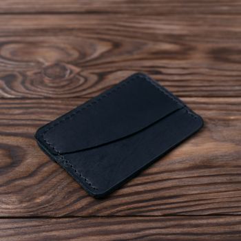 Black colour handmade leather one pocket cardholder on wooden background. Stock photo with soft blurred background.