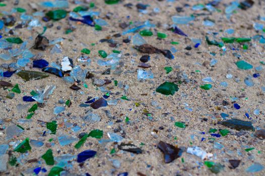Broken glass bottles on white sand. Bottles is green and blue colour. Trash on the sand. Ecological problem.