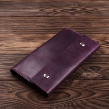 Purple handmade travel wallet lies on textured wooden backgroud closeup. Side view. Stock photo of businessman accessories.