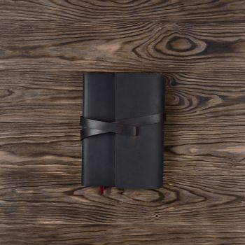 Dark brown handmade leather notebook cover with notebook on wooden background. Stock photo of luxury business accessories. Up to down view.