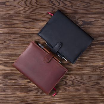 Black and brown handmade leather notebook cover with notebooks and pen on wooden background. Stock photo of luxury business accessories. Up to down view.