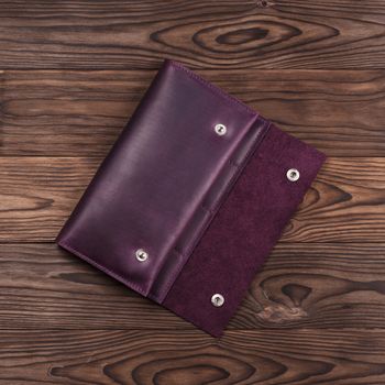 Purple handmade travel wallet lies on textured wooden backgroud closeup. Up to down view. Stock photo of businessman accessories.