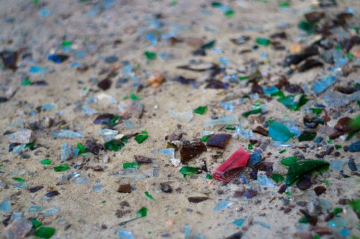 Broken glass bottles on white sand. Bottles is green and blue colour. Trash on the sand. Ecological problem.