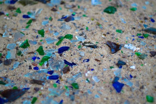 Broken glass bottles on white sand. Bottles is green and blue colour. Trash on the sand. Ecological problem.