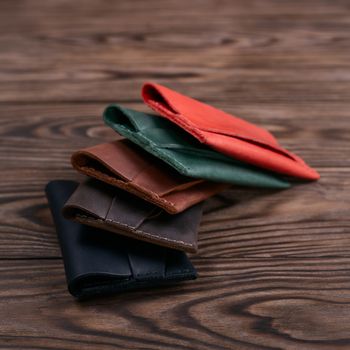 Five handmade leather cardholders on wooden background lie one on another. Stock photo with blurred background.