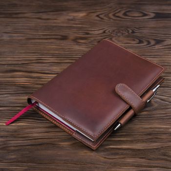 Red color handmade leather notebook cover with notebook and pen inside on wooden background. Stock photo of luxury business accessories.