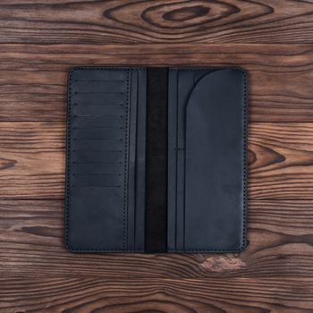 Handmade black travel wallet lies on textured wooden backgroud closeup. Wallet is open and empty. Up to down view. Stock photo of businessman accessories.