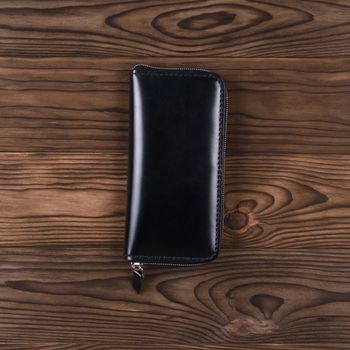 Gloss black color handmade leather porte-monnaie on wooden textured background.  Up to down view. Stock photo of luxury accessories.