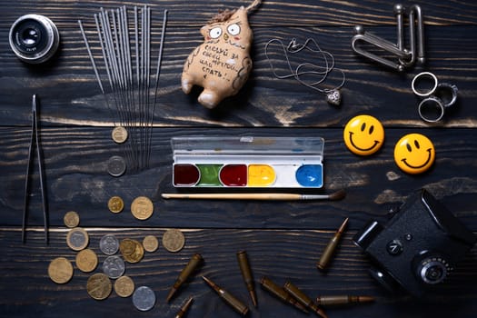 Flat lay wooden charred background. On wooden boards lies bengali fire, silver pendant, tweezers, toy, rings, coins, brush and paint, ammo, smiling magnets, camera prism and old lens.