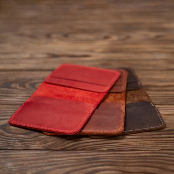 Three leather cardholders lies one another one on wooden background. Red, ginger and brown cardholders on photo. Stock photo with blurred background.