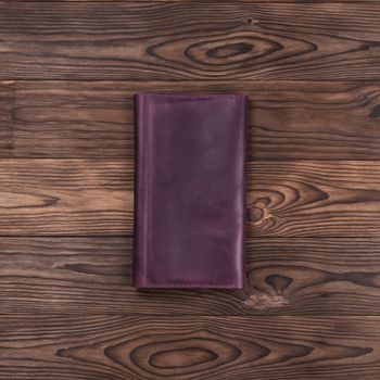 Purple handmade travel wallet lies on textured wooden backgroud. Up to down view. Stock photo of businessman accessories.