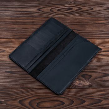 Handmade black travel wallet lies on textured wooden backgroud closeup. Wallet is open and empty. Side view. Stock photo of businessman accessories.