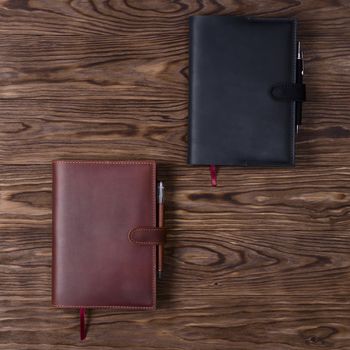 Black and brown handmade leather notebook cover with notebooks and pen on wooden background. Stock photo of luxury business accessories. Up to down view.