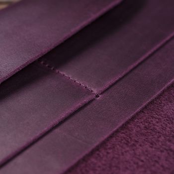 Part of purple handmade travel wallet lies on textured wooden backgroud closeup. Wallet is open and empty. Side view. Stock photo of businessman accessories.