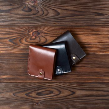 Three handmade leather wallets on wooden textured background. Up to down view. Wallet stock photo.