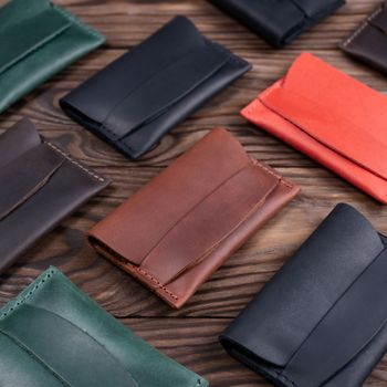 Flat lay photo of five different colour handmade leather one pocket cardholders. Red, black, blown, ginger and green colors. Stock photo on wooden background.