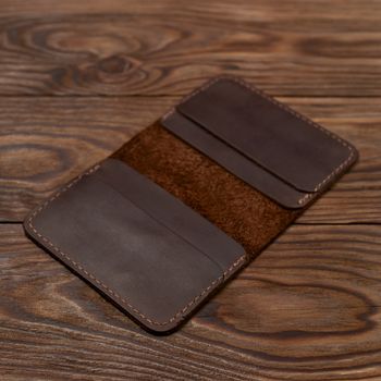 Handmade brown leather cardholder on wooden background. Cardholder have 4 pockets for cards. Stock photo with soft focus background.