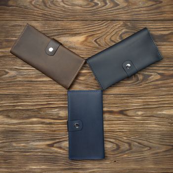 Three handmade leather wallets on textured wooden background. Wallet is unisex. Up to down view. Stock photo of luxury accessories.