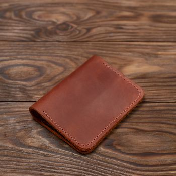 Ginger colour two-pocket closed leather handmade cardholder lies on wooden background. Soft focus on background. Stock photo on blurred background.