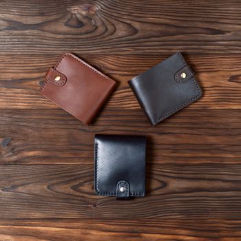 Three handmade leather gloss wallets on wooden textured background. Up to down view. Businessman wallet stock photo.
