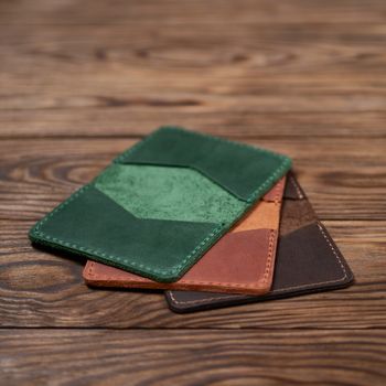 Three leather cardholders lies one another one on wooden background. Green, ginger and brown cardholders on photo. Stock photo with blurred background.