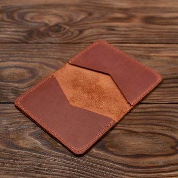 Handmade ginger leather cardholder on wooden background. Stock photo with blurred background.