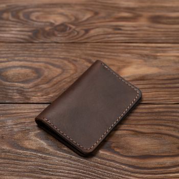 Brown two-pocket closed leather handmade cardholder lies on wooden background. Soft focus on background. Stock photo on blurred background.