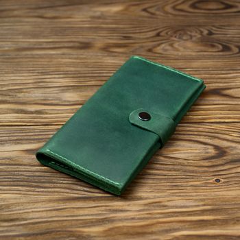 Green color handmade leather wallet on textured wooden background. Wallet is unisex. Side view. Stock photo of luxury accessories.