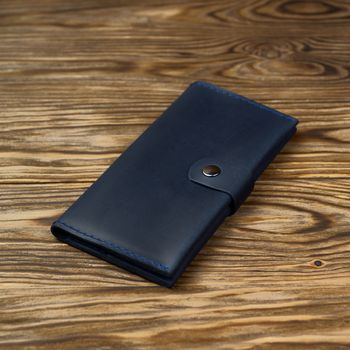 Dark blue color handmade leather wallet on textured wooden background. Wallet is unisex. Side view. Stock photo of luxury accessories.
