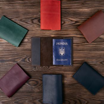 Six handmade leather passport covers around one opened cover on wooden textured background. Up to down view. Stock photo of luxury accessories.