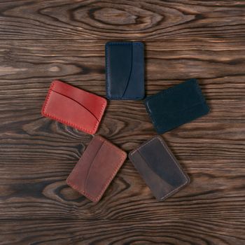 Five handmade leather cardholders on wooden background lies star shaped. Stock photo on perfect wooden background. Blue, black, brown, ginger and red items on photo.