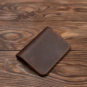 Brown two-pocket closed leather handmade cardholder lies on wooden background. Soft focus on background. Stock photo on blurred background.