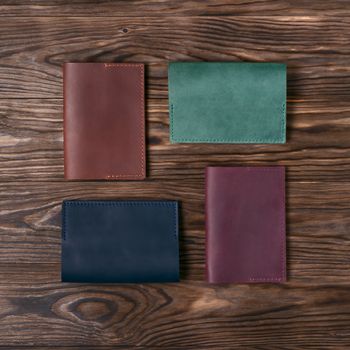 Four handmade leather passport covers on wooden textured background. Up to down view. Stock photo of luxury accessories.