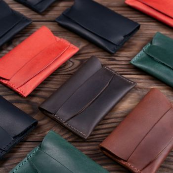 Flat lay photo of five different colour handmade leather one pocket cardholders.  Red, black, blown, ginger and green colors. Stock photo on wooden background.
