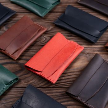 Flat lay photo of five different colour handmade leather one pocket cardholders.  Red, black, blown, ginger and green colors. Stock photo on wooden background.