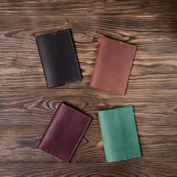 Four handmade leather passport covers on wooden textured background. Up to down view. Stock photo of luxury accessories.