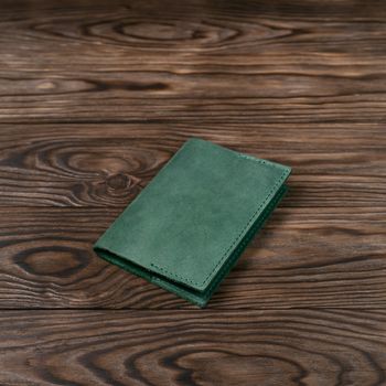 Mattle green color handmade leather passport cover on wooden textured background. Businessman`s accessory.