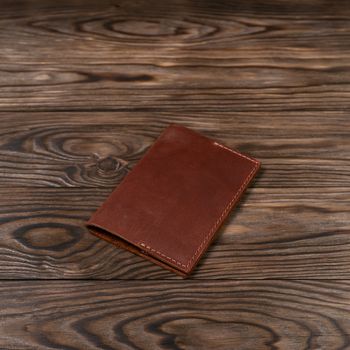 Ginger color handmade leather passport cover on wooden textured background. Businessman`s accessory.