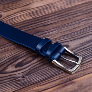 Hue blue handmade belt buckle lies on textured wooden background closeup. Side view. Stock photo of businessman accessories.