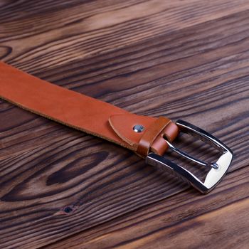 Hue ginger color handmade belt buckle lies on textured wooden background closeup. Side view. Stock photo of businessman accessories.