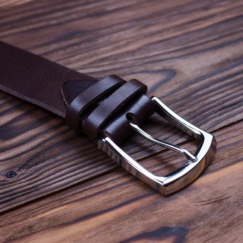 Brown handmade belt buckle lies on textured wooden background closeup. Side view. Stock photo of businessman accessories.