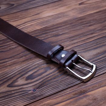 Brown handmade belt buckle lies on textured wooden background closeup. Side view. Stock photo of businessman accessories.