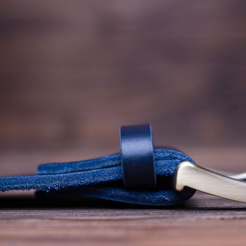 Blue handmade belt buckle lies on textured wooden background closeup. Side view. Stock photo of businessman accessories with blurred background.