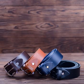 Four handmade belts lies on textured wooden background closeup. Belts are twisted into a ring. Side view. Stock photo of businessman accessories.