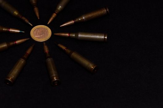 Rifle ammo around one euro coin on black background. Symbolizes the war for money and one of the world's problems.