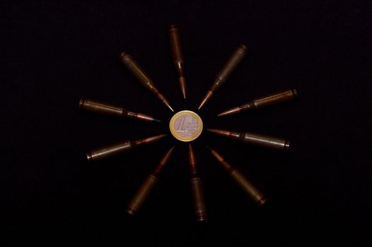 Rifle ammo around one euro coin on black background. Symbolizes the war for money and one of the world's problems.