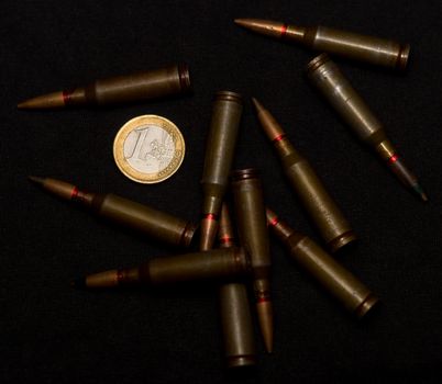 Rifle ammo around one euro coin on black background. Symbolizes the war for money and one of the world's problems.