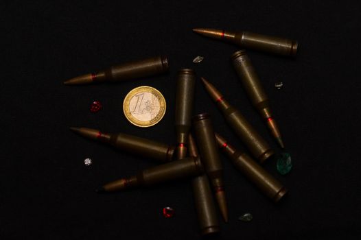 Rifle ammo around one euro coin wigh gemstones on black background. Symbolizes the war for money and one of the world's problems.