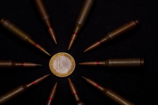 Rifle ammo around one euro coin on black background. Symbolizes the war for money and one of the world's problems.